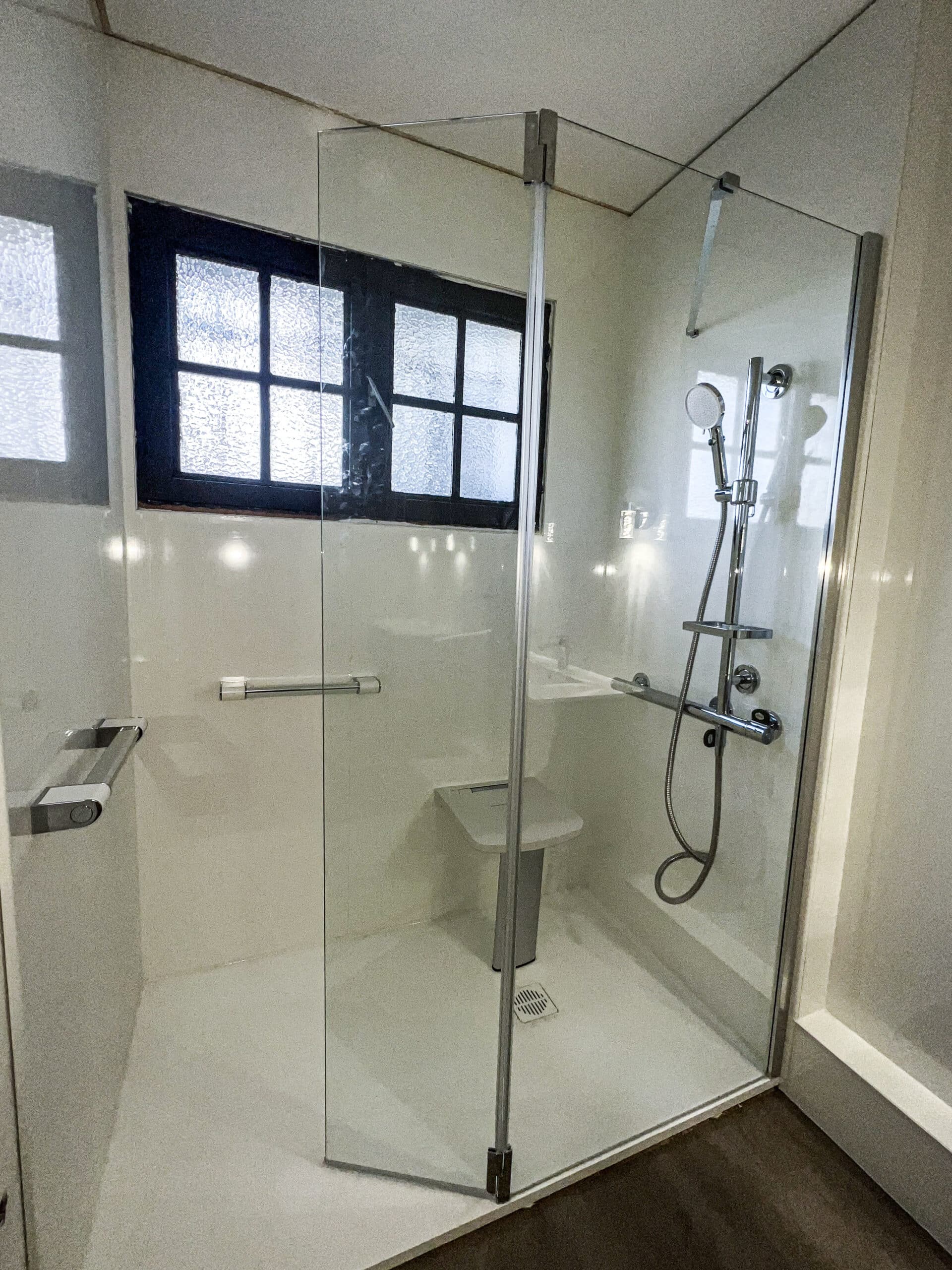 Douche accessible moderne avec cabine en verre, siège rabattable, barres d'appui chromées et fenêtres dépolies.