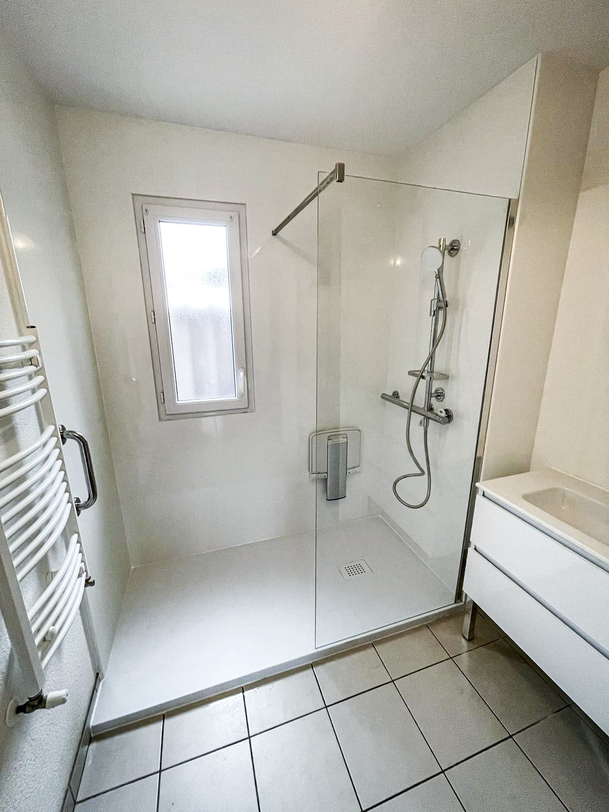 Salle de bain moderne lumineuse avec douche à l'italienne, paroi vitrée, siège pliable, radiateur sèche-serviettes blanc et meuble vasque.