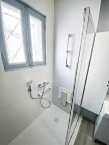 Douche moderne avec siège rabattable et pommeau, fenêtre à vitrage texturé, murs bicolores gris/blanc et cabine en verre.