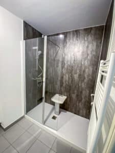 Salle de bain moderne: douche à l'italienne vitrée, murs gris texturés, receveur blanc, lavabo d'angle et sèche-serviettes.