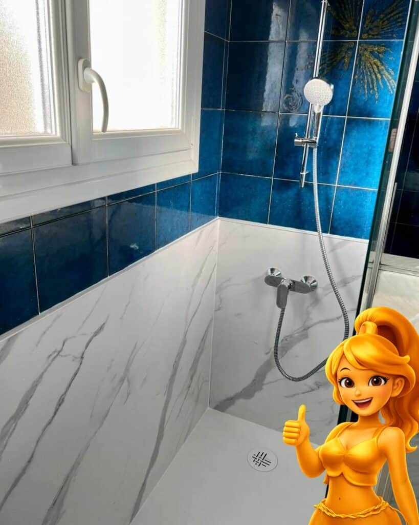 Douche design : carrelage bleu vibrant et panneaux effet marbre blanc veiné. Fenêtre givrée. Personnage doré lève le pouce.