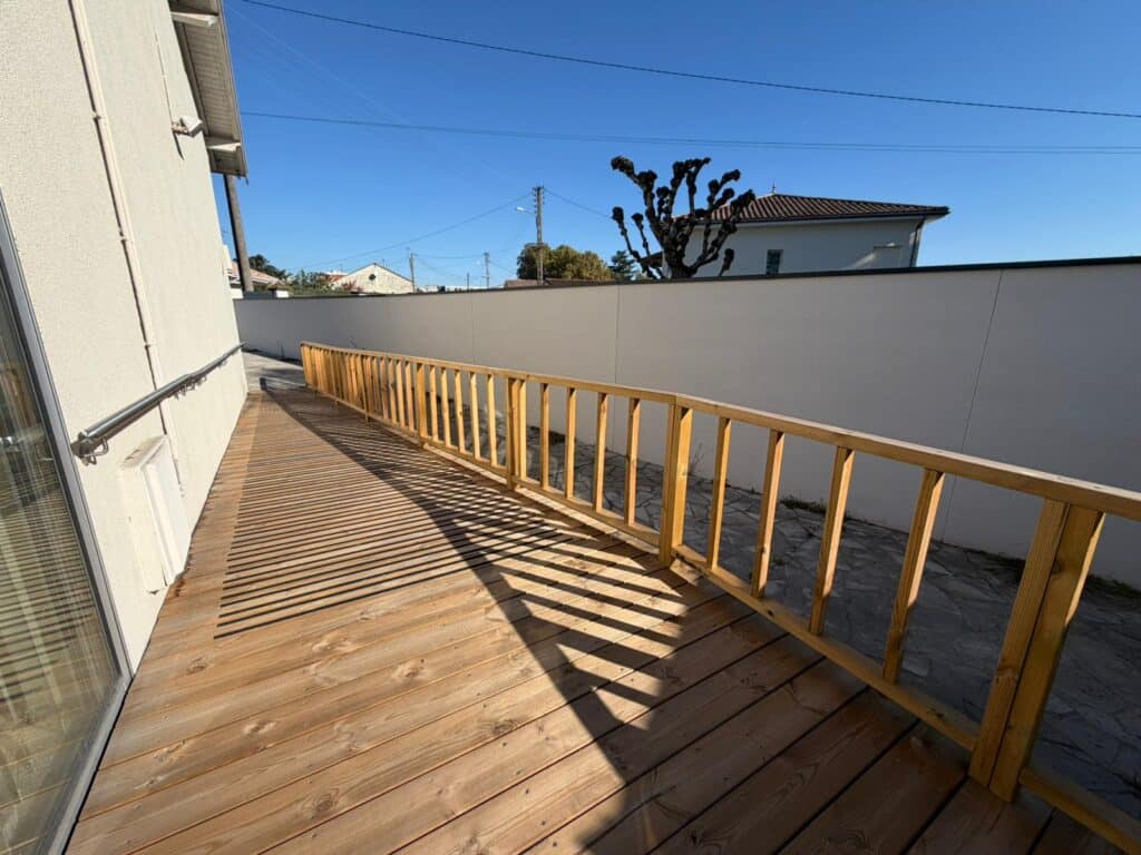 Large rampe d'accès en bois pour PMR, éclairée par le soleil. Main courante en acier inoxydable et garde-corps en bois. Ombres portées.