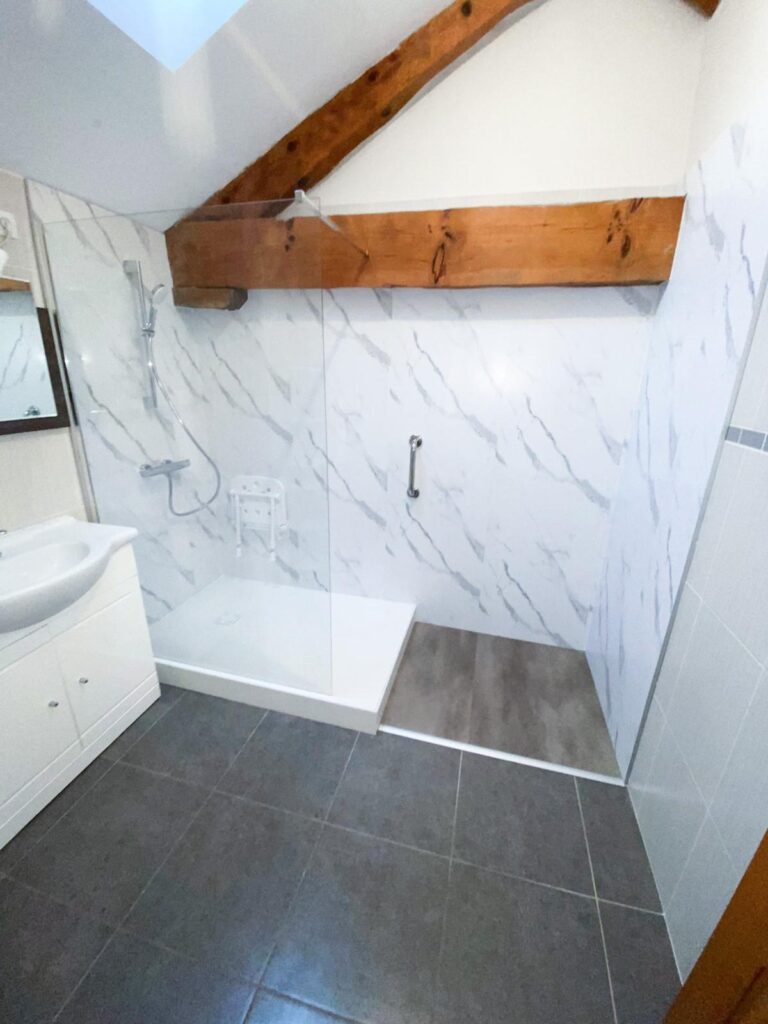 Douche PMR accessible design avec murs effet marbre Douche à l'italienne avec parois effet marbre, poutre bois apparente et siège PMR dans une salle de bain moderne.