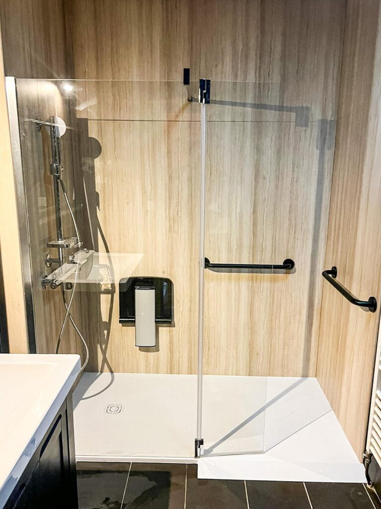 Douche accessible moderne avec barres d'appui noires Douche accessible moderne avec barres d'appui noires, paroi vitrée et carrelage mural aspect bois.