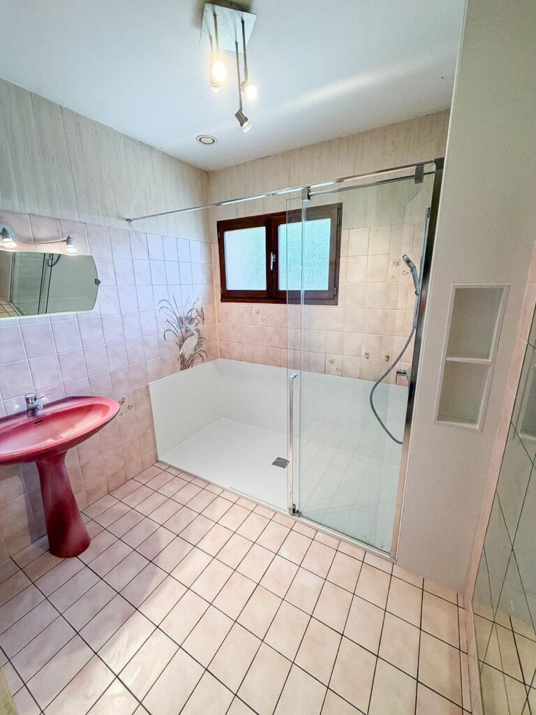 Salle de Bain Rétro : Carrelage Rose et Lavabo Rouge Salle de bain rétro avec carrelage rose, lavabo colonne rouge et douche à l'italienne spacieuse.