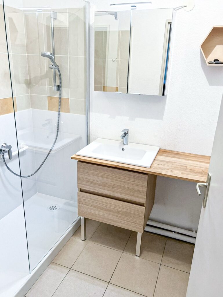 Salle de bain moderne : douche et meuble vasque en bois Salle de bain moderne avec douche à l'italienne vitrée, meuble vasque en bois clair et armoire à miroir.