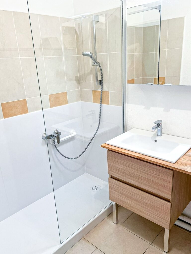 Salle de bain moderne avec douche à l'italienne, paroi vitrée et meuble sous-vasque en bois clair.